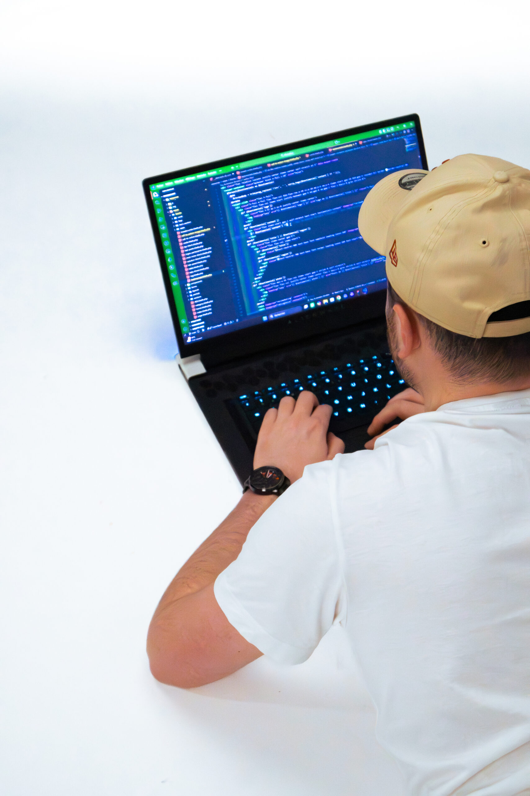 Photo d’un développeur web de dos en train de coder sur un ordinateur portable, sur fond blanc minimaliste.